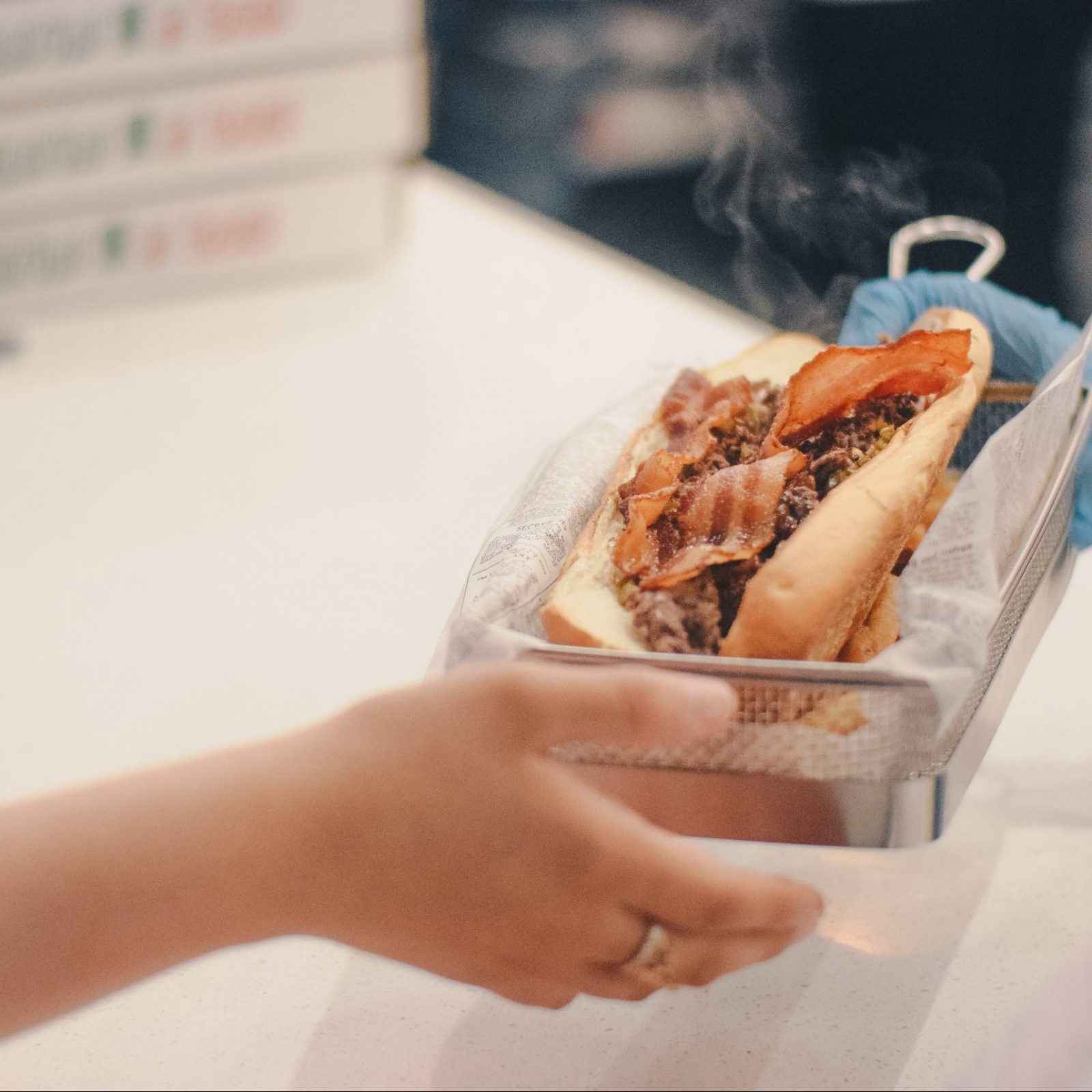 A person's hand holding a Tono cheesesteak in a basket